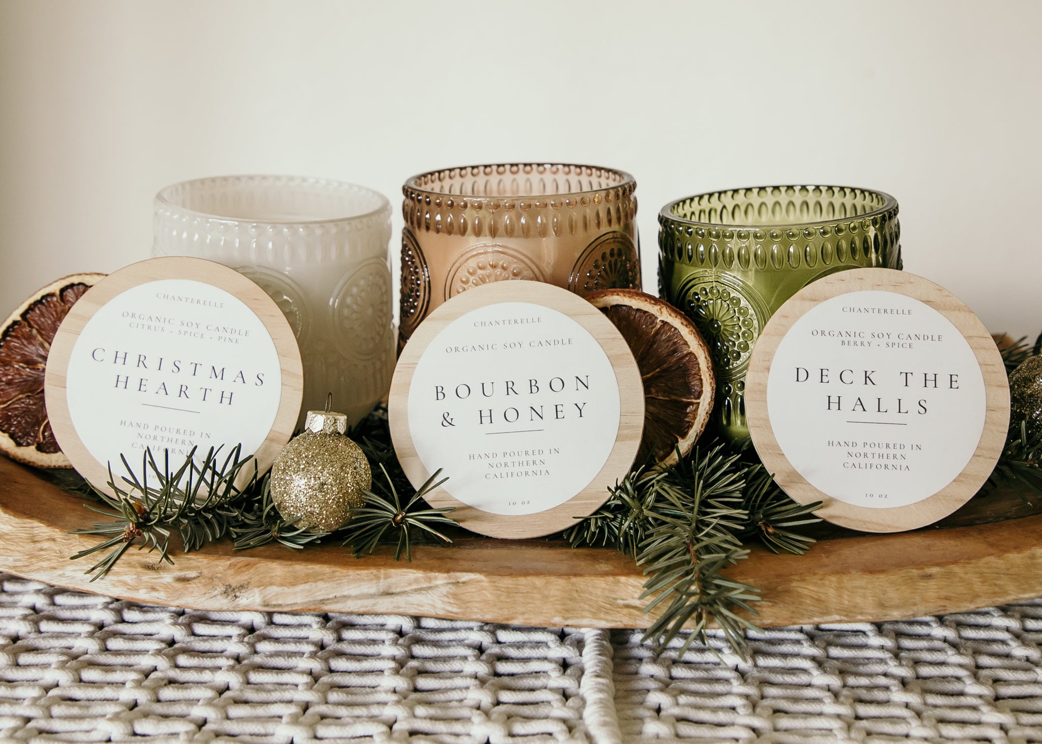 Set of candles with decorative labels on a wooden surface with greenery