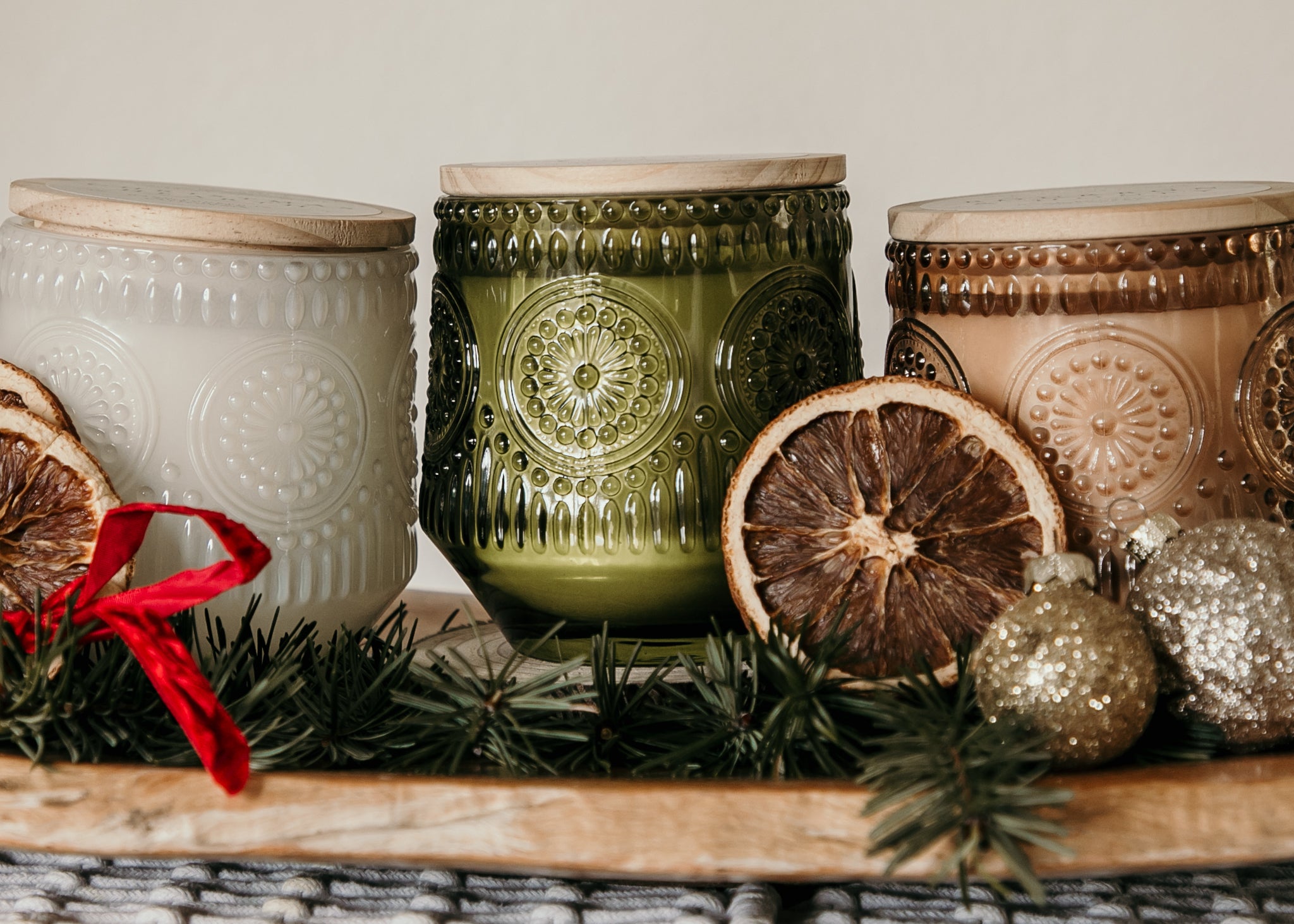 Three decorative candles with textured surfaces and holiday elements on a wooden surface.